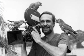 filmmaker Bodanzky, holding movie camera with parrots perched on his arm and camera, black and white